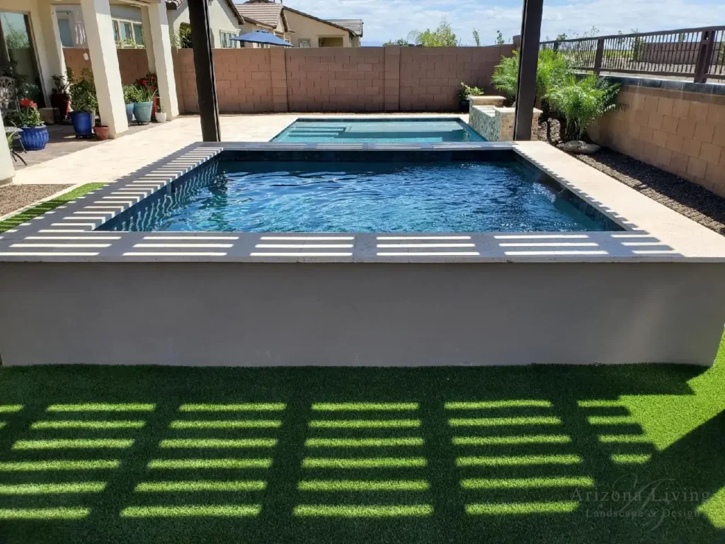 Modern backyard pool with raised koi pond, pergola shade, and artificial turf in Eastmark -Mesa, AZ — designed by Arizona Living Landscape & Design