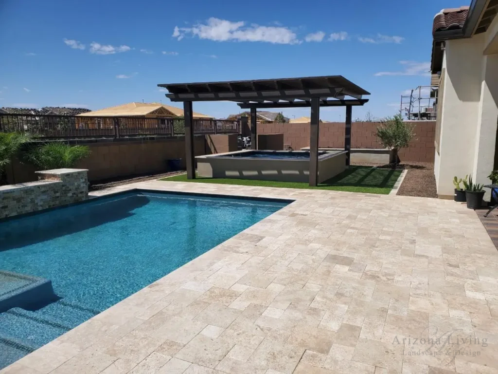 Backyard pool with travertine paver deck, with pergola shade over koi poind, synthetic turf, garden planter, and plants in Eastmark -Mesa, AZ — designed by Arizona Living Landscape & Design.