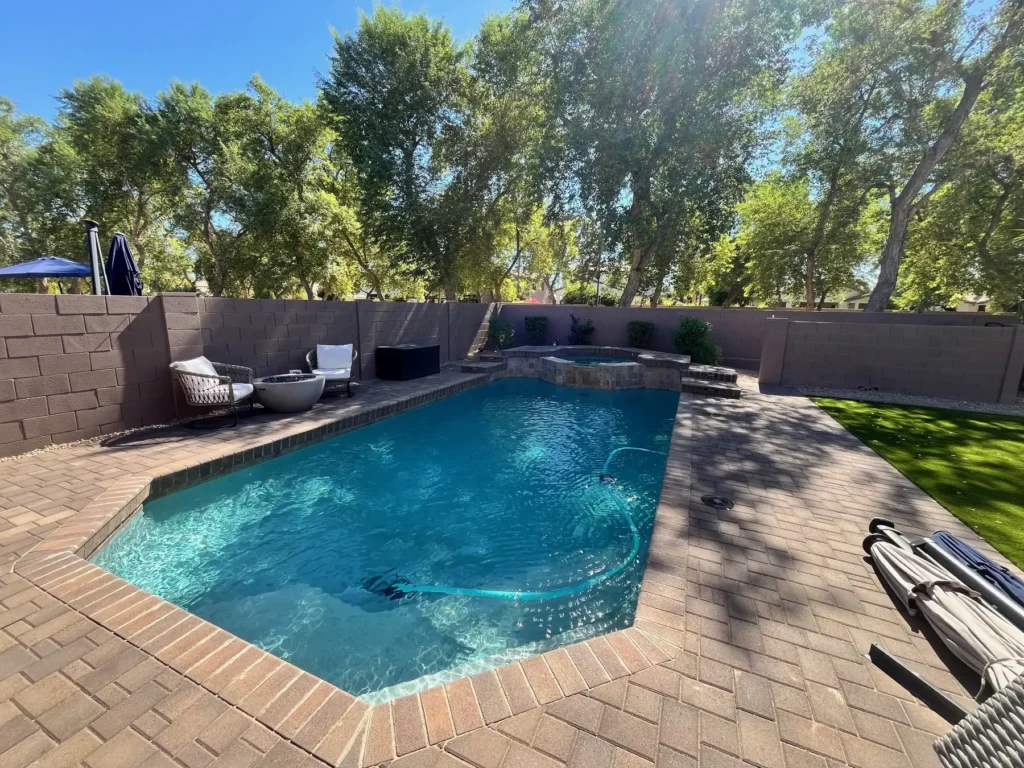 “Custom backyard pool with travertine paver deck, spa, and artificial turf in Queen Creek, AZ by Arizona Living Landscape & Design.”